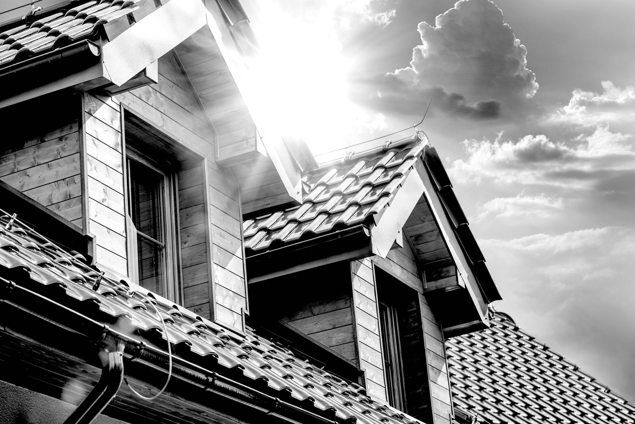 A house roof with two dormer windows and the sun shining between them