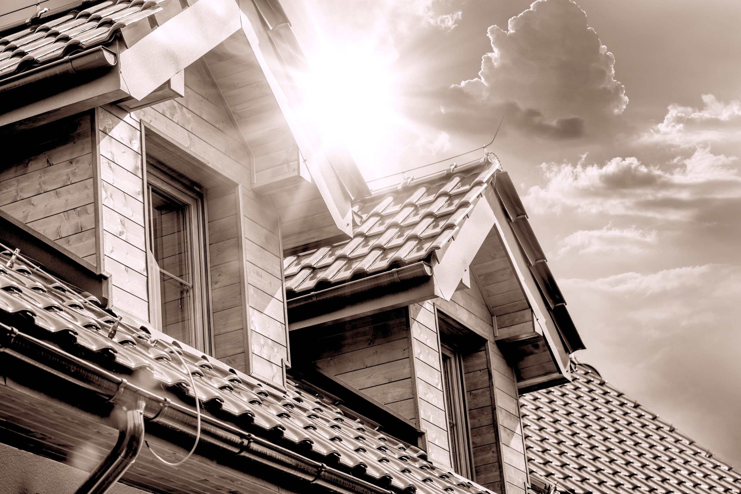 A house roof with two dormer windows and the sun shining between them