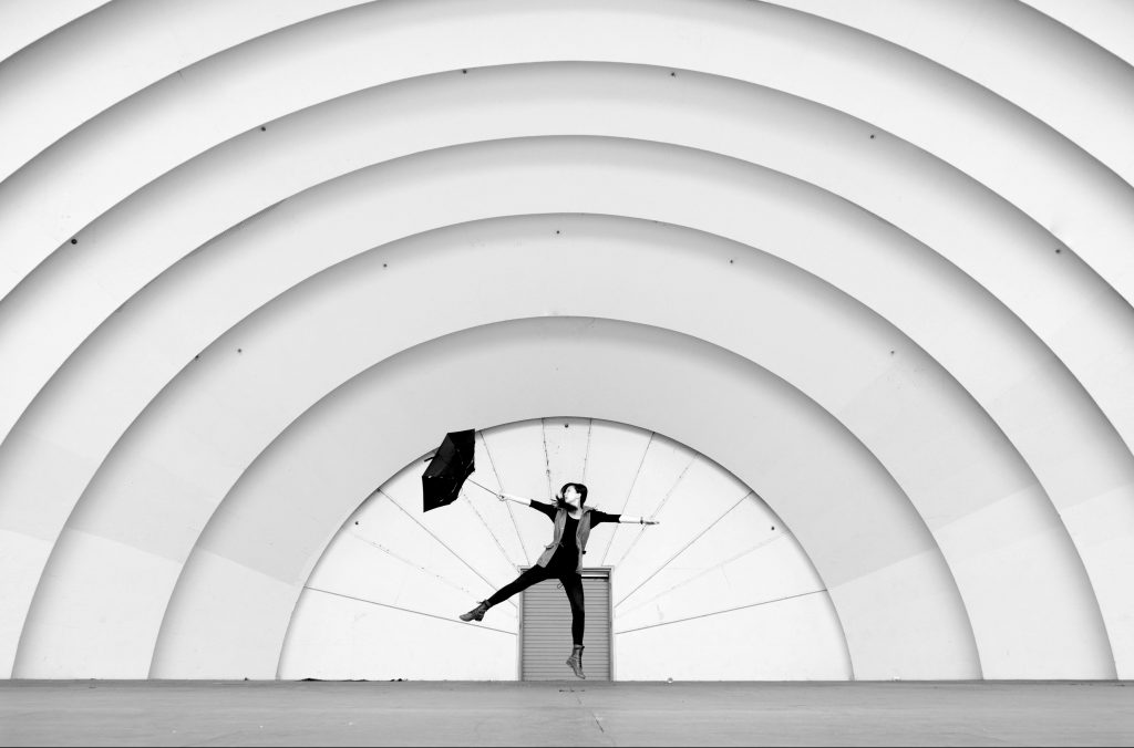 Person with umbrella jumping in front of a building