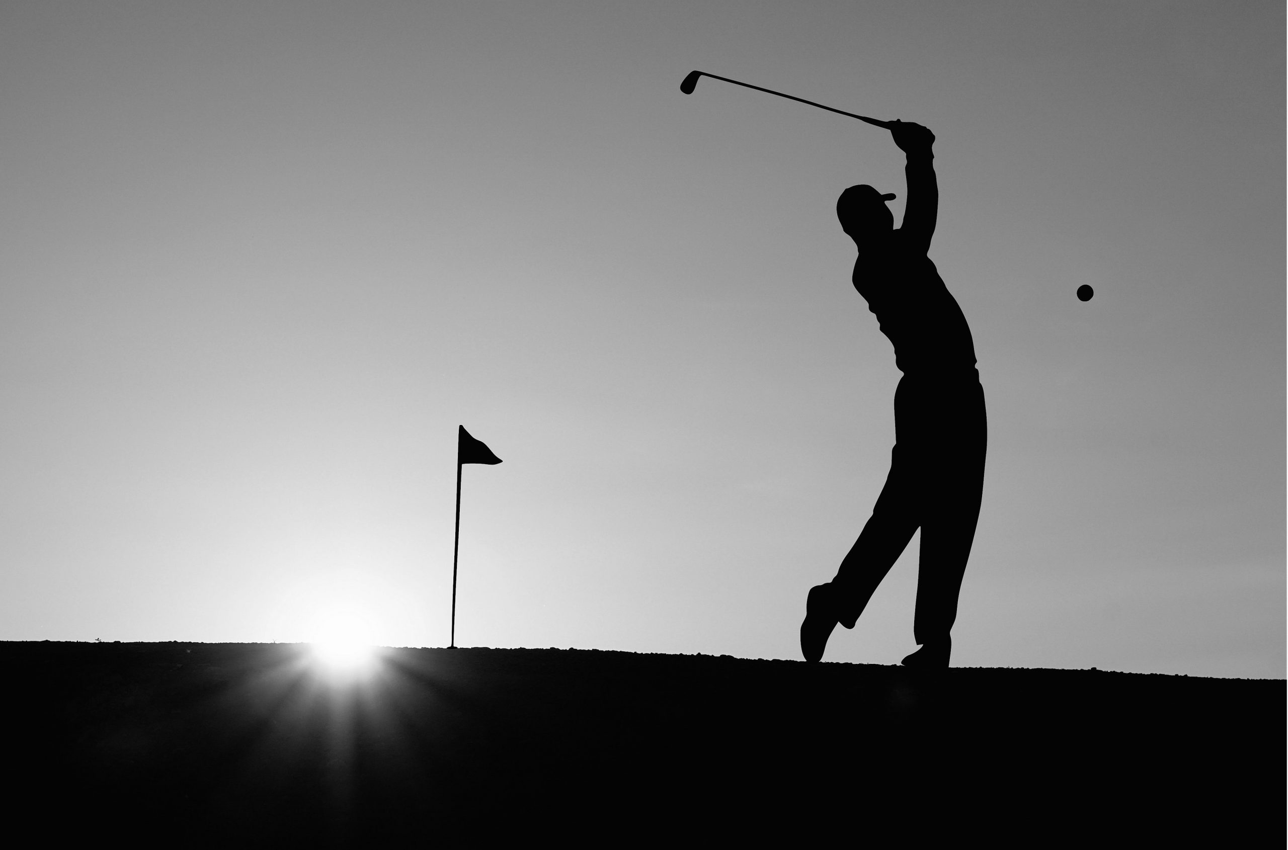 Golfer, flag and golf ball in silhouette against sunset