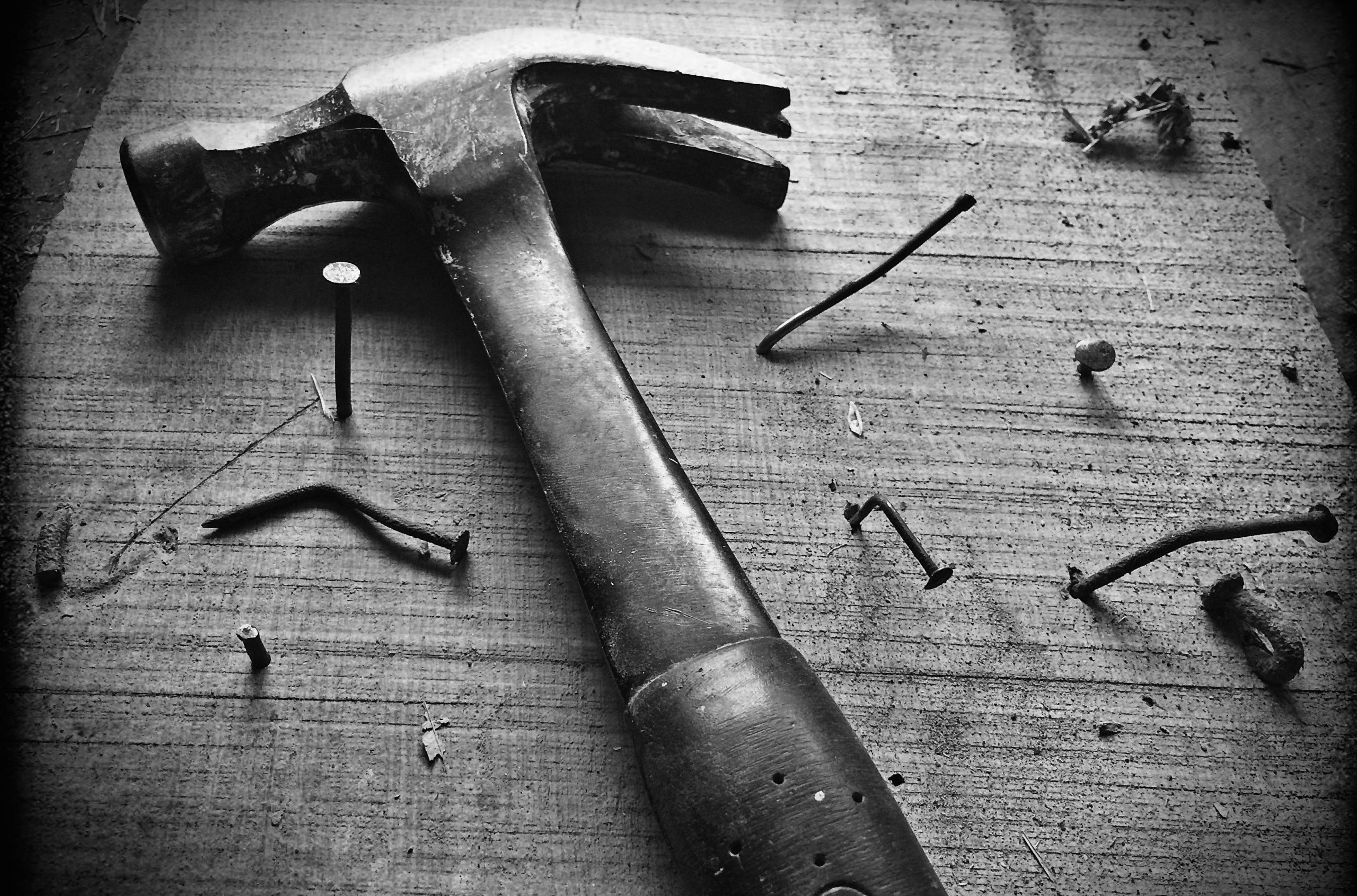 Hammer lying on wooden board with several bent nails in